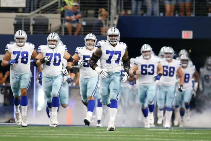 Tyron Smith runs out onto the field leading a group of Cowboys players out of the tunnel behind him with smoke at their feet